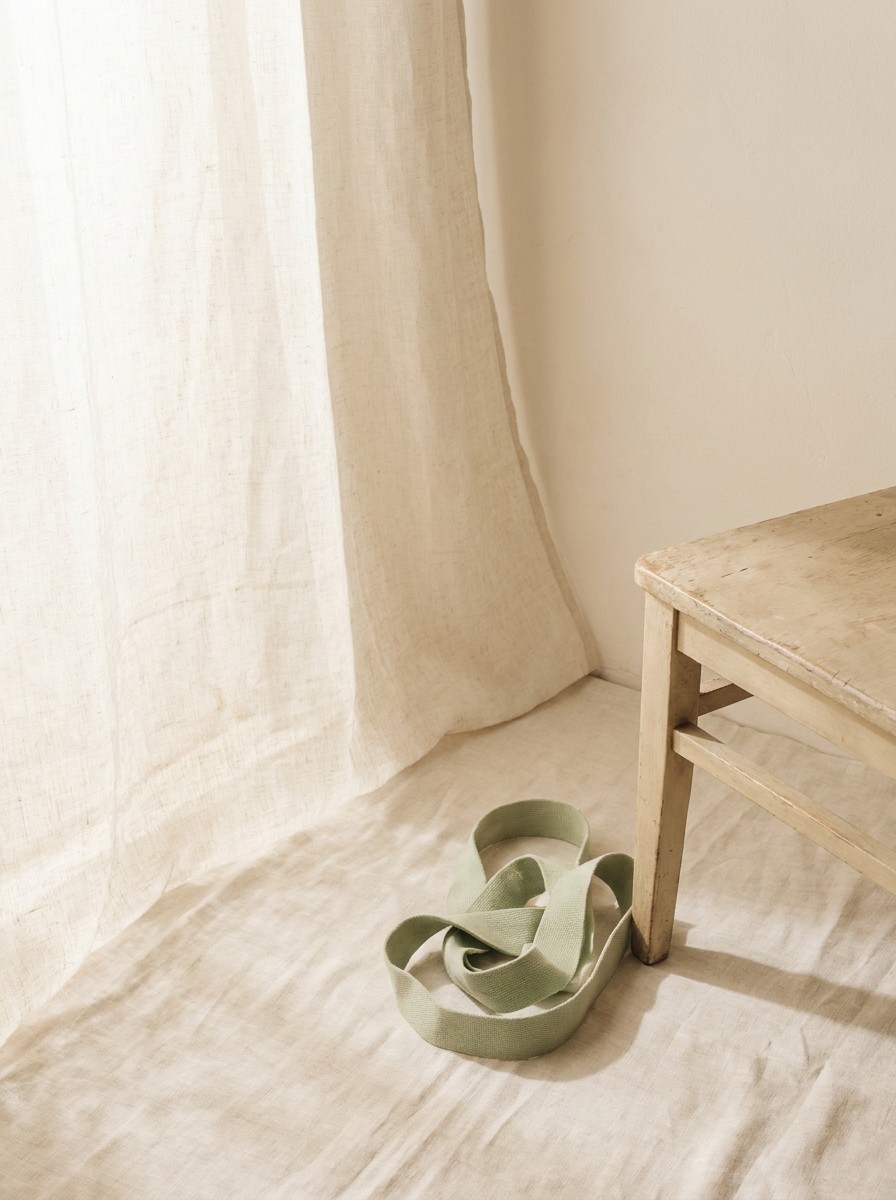 The corner of a plain wooden chair and a coiled pale green resistance band at the lower-right, with bright empty space at the upper-left.