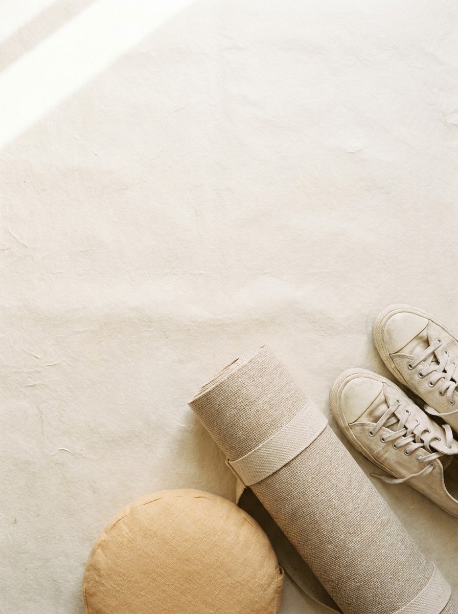 A rolled linen yoga mat, a round cushion and a pair of canvas sneakers at the lower-right of cream hanji paper, with bright empty space at the upper-left.