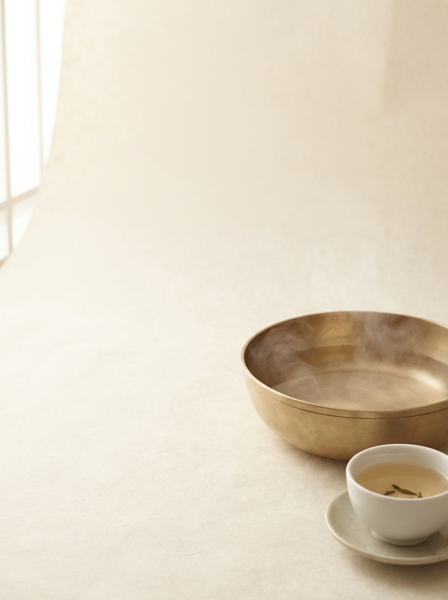 A shallow brass basin of steaming warm water and a small cup of warm tea pushed to the lower-right of a hanji surface, the upper-left left empty.