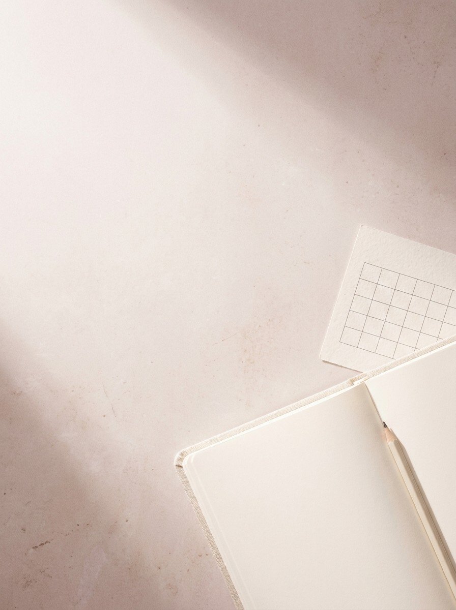 An open blank notebook with a pencil and a blank paper calendar on pale stone, upper left of the frame left empty