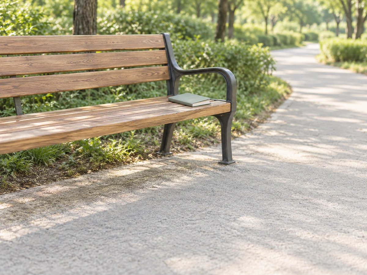 An empty wooden park bench beside a walking path with a closed blank record notebook resting on one end