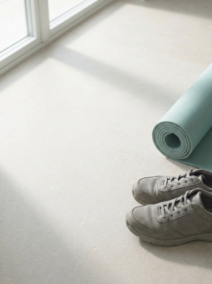 A pair of plain grey walking shoes and a rolled teal exercise mat at the lower right of pale stone, upper left of the frame left empty