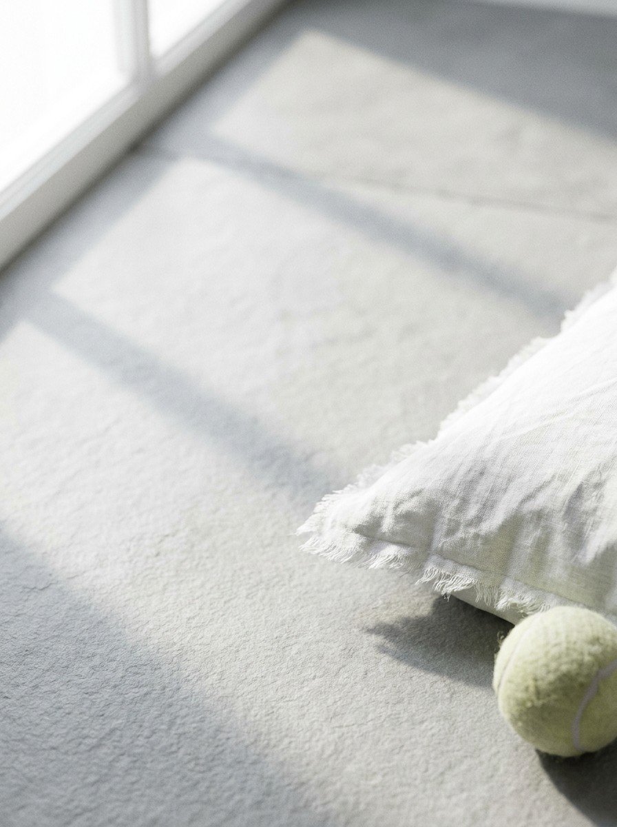 The corner of a white linen pillow and a pale tennis ball in the lower right of light slate stone, upper left empty