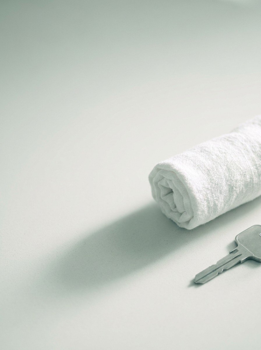 A rolled white towel and a plain car key at the lower right of pale stone, upper left of the frame left empty